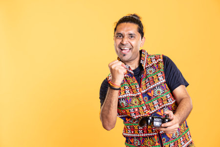 Cheerful gamer clutching fist, celebrating after winning game on gaming console, studio background. Overjoyed man bragging after being victorious in videogame, defeating all players using gamepadの写真素材