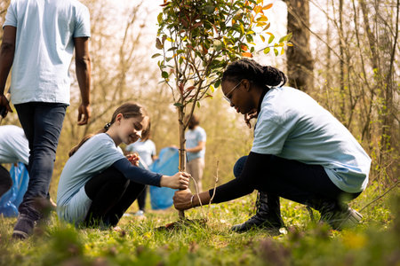 Two diverse girls working together to plant more seedlings and greenery, filling up ground holes and growing vegetation. Child and teenager collaborating on protecting the forest ecosystem.の写真素材