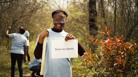 Portrait of african american activist holding poster with save our planet message, spread environmental care and awareness. Young woman posing with banner to fight ecological justice. Camera B.の写真素材