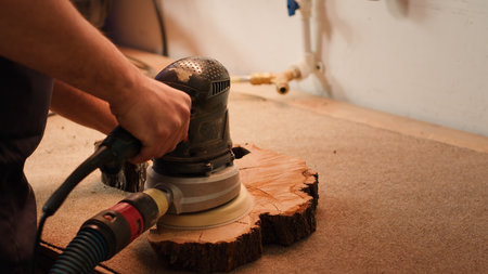Carpenter using angle grinder on timber block to smooth surfaces with sandpaper. Woodworking professional using orbital sander equipment for furniture assembling job in studio, close up, camera Aの写真素材