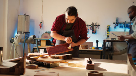 Carpenter in assembly shop starting restoration project on lumber block, applying lacquer on surface. Woodworking specialist coloring wood plank with paintbrush, doing handwork in studio, camera Bの写真素材