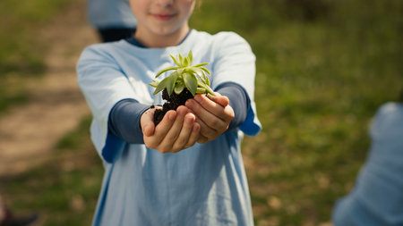 Small child holding soil with a green sprout in her hands, contributing to environmental preservation and natural cultivation. Young activist doing voluntary work to save the planet. Camera A.の写真素材