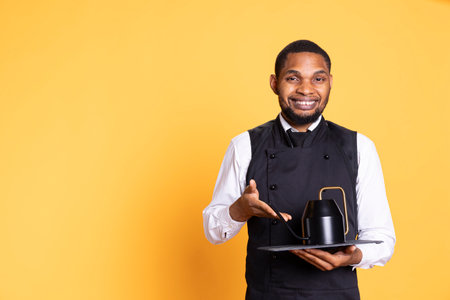 Skilled waiter bringing the teapot to the clients table to serve them tea before their meal order, service oriented industry. Employee with apron serves customers for satisfaction.の写真素材