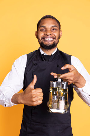 Catering employee showing a thumbs up gesture in studio, presenting his approval and content emotions on camera. Young restaurant waiter gives a like sign, professionalism.の写真素材