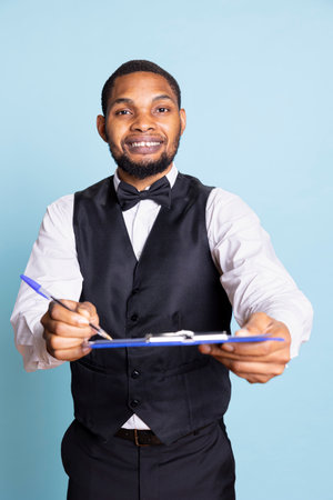 Hotel worker writing down notes on clipboard files against blue background, ensuring easy check in process for guests. Bellboy providing excellent concierge services, hospitality industry.の写真素材