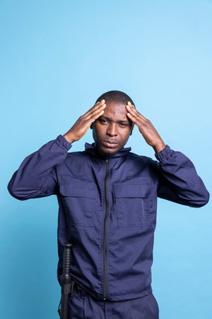 African american security officer is feeling sick and gloomy with a painful migraine, dealing with stress and pressure from his duty. Unhappy patrol agent with anxiety, bad symptoms.の写真素材