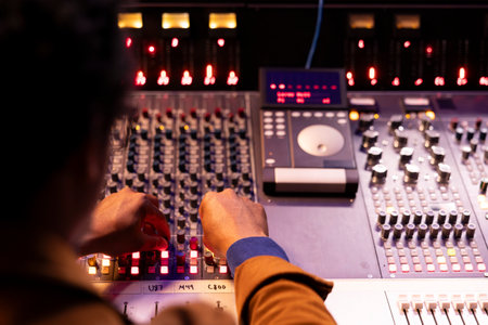 African american audio technician pushing sliders and switchers on panel board in control room,...