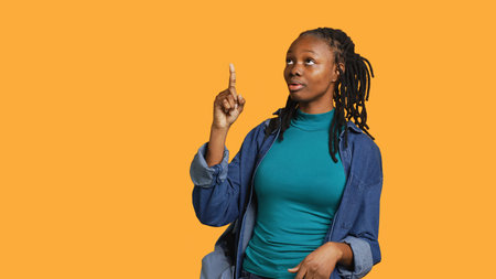 African american woman pointing with finger in all directions, talking with audience. Young teenager doing presentation, showing copy text, studio backdrop, camera Aの写真素材