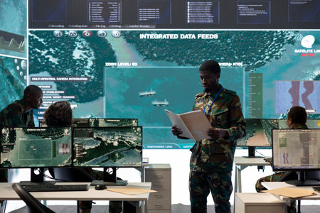 Special operations engineer reading new mission case file brief in control room, working with real time surveillance projection on a big screen. Trooper in army division defense program.の写真素材