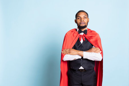 African american doorman posing in a superhero red mantle in studio, acting as a hero and savior for the clients. Happy confident bellhop with a superhuman cape, professionalism.の写真素材