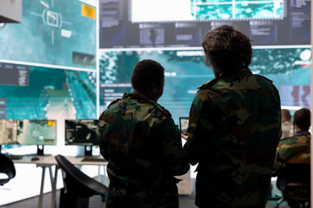 Diverse team of military personnel analyzing battlefield real time data on CCTV radar satellite system, transmitting information to soldiers in the field. Army superiors work on defense program.の写真素材