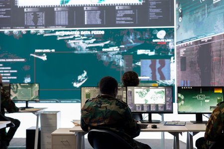 Army staff examining surveillance footage on big screen in operation room, gathering intelligence for a new defense mission. Diverse group of troopers working on reconnaissance activity.の写真素材