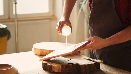 Woodworking specialist applying varnish on wood to build up protective layer. Cabinetmaker in assembly shop lacquering wooden board after sanding surface to ensure smoothness, close up shot, camera Aの写真素材