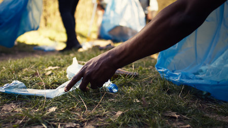 People supporting cleanup of the natural environment by grabbing recyclables and trash objects from the woods, collecting in a garbage bag. Using utensils to pick up rubbish. Close up. Camera B.の写真素材
