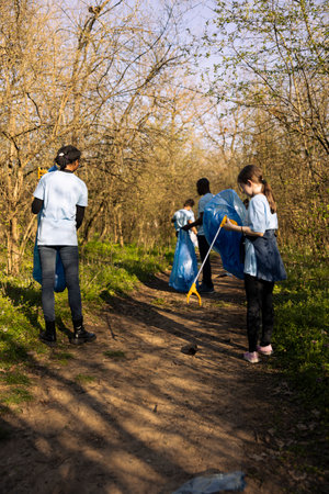 Environmental activist child gathering junk and plastic waste with a claw tool, recycling rubbish and clearing the forest. Young girl supporting ecology and zero waste activism.の写真素材