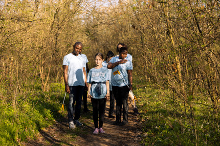Team of activists tidying up the woodland by collecting junk in bags, recycling plastic bottles for a sustainable lifestyle. Volunteers picking up trash and fighting against pollution.の写真素材