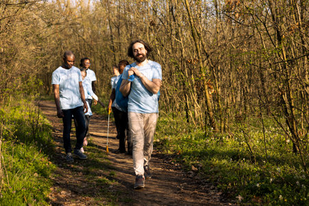 Pleased group of activists finishing litter cleanup in a forest area, grabbing their garbage...