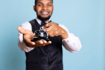 Bellboy personnel using the service bell to provide his services and help the hotel guests, wearing a suit and tie as uniform. Receptionist working at a five star holiday resort, tourism.の写真素材