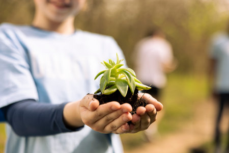 Little girl holding small grown tree seed with soil in her hands, fighting to protect the natural forest ecosystem. Small child activist fixing pollution and conserving nature by planting more trees.の写真素材