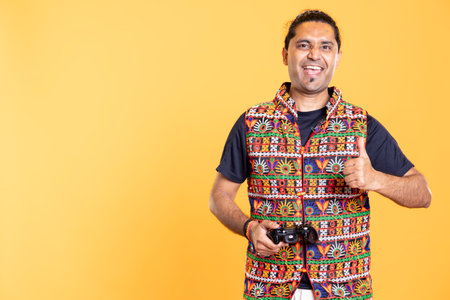Cheerful gamer showing thumbs up sign gesturing holding controller, playing videogames. Joyful person excited to do gaming, doing approving hand gesture, studio backgroundの写真素材