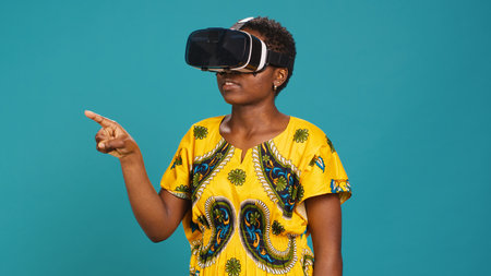 Gorgeous girl in ethnic clothes using vr glasses against blue background, working with high tech 3d experience with virtual reality device. Young woman using smart headset. Camera A.の写真素材