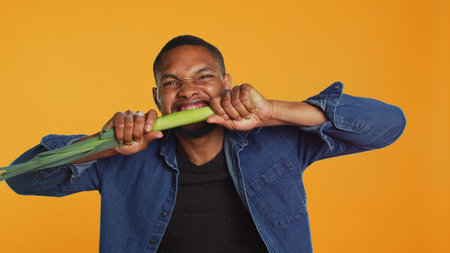 Young person biting on a green onion and acting silly in studio, pretending to eat a leek to advocate for lifestyle and veganism.の写真素材