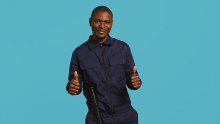 Portrait of joyous security guard doing thumbs up sign gesturing with finger while overseeing premises. Private law enforcement worker doing positive hand gesture, studio backdrop, camera Bの写真素材