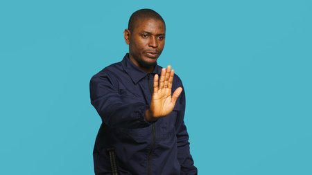 Portrait of security guard doing stop sign gesturing to intruder while overseeing premises. Private law enforcement worker showing halt hand gesture to trespasser, studio backdrop, camera Aの写真素材