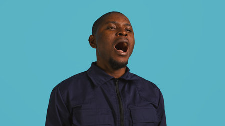 Portrait of security job employee yawning while at work detaining perpetrators, feeling tired. Patrol guard feeling exhausted after long night shift, isolated over studio background, camera Bの写真素材