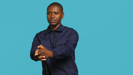 Portrait of security staff member tasked with evicting trespassers, pretending to shoot gun. Patrolling agent maintains secure environment, doing pistol fingers gesturing, studio background, camera Aの写真素材