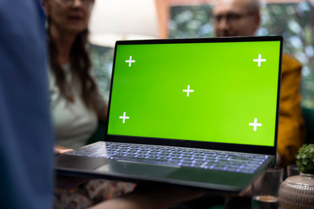 Caretaker offers professional advice to her elderly patients next to green screen on laptop, consulting senior couple during a home visit. Medical assistant provides support and medication.の写真素材