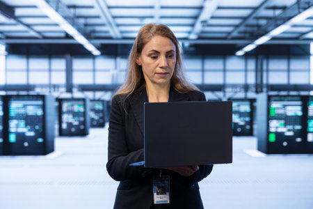 Technician in data center implementing backup solutions to protect against data loss using notebook, ensuring efficient recovery processes. Server hub worker identifying and resolving technical issuesの写真素材