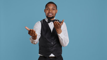 Bellhop doorkeeper ringing the service bell to present his help and assistance upon the guests arrival, blue background. Hotel porter providing great luxury services at resort. Camera B.の写真素材