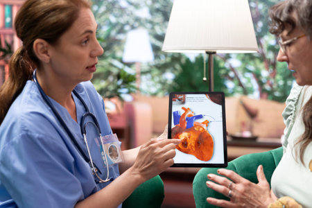 Skilled nurse explaining a heart condition or disease to elderly patients, cardiovascular system illustration during checkup visit at home. Healthcare and senior support for healthy recovery.の写真素材