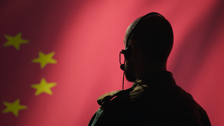 Military dispatcher working for Chinese Communist Party providing informations for troops using headset. Radio communications operator isolated over China flag background coordinating troops, camera Bの写真素材