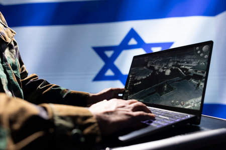 IDF military operative uses laptop to analyze surveillance data, standing isolated over Israel flag background. Close up shot of soldier engaged in geopolitical operation, protecting bordersの写真素材