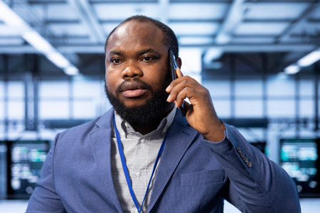 Team leader overseeing operations in modern data center, coordinating tasks during phone call. Close up of IT professional in server farm managing systems and communicating via smartphoneの写真素材