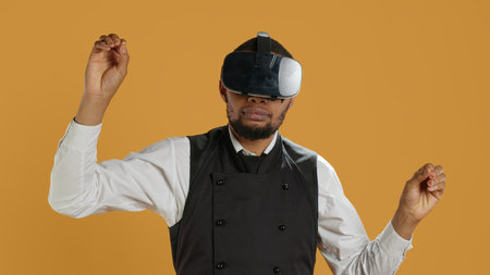 Restaurant waiter uses virtual reality headset with artificial intelligence, having fun with technology and vr glasses against yellow background. Employee with apron and uniform. Camera A.の写真素材