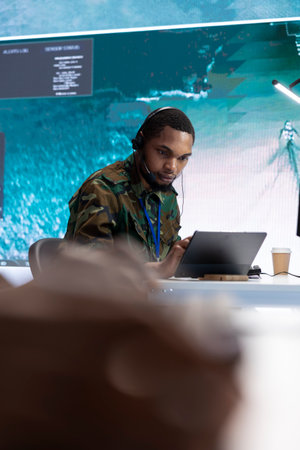 Military crew in a high tech control center working with real time data, supervising cctv satellite systems on a computer. Working with big screen in a command post for defense missions.の写真素材
