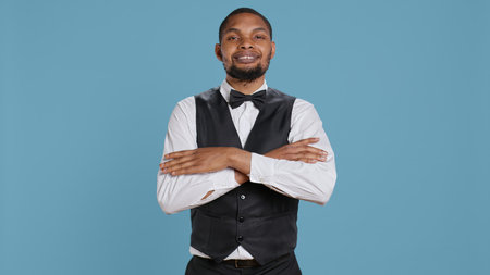 Portrait of bellhop hotel employee posing with arms crossed, showing confidence and professionalism dressed in a tuxedo and tie. Doorkeeper bellboy works in hospitality industry. Camera B.の写真素材
