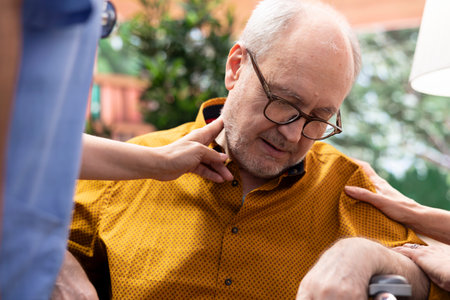 Caregiver helping elderly man in wheelchair losing conscience during checkup visit, old person hyperventilating and scaring his wife. Medical nurse in panic checking the pulse. Close up.の写真素材