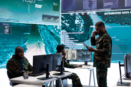 Military team in a command center uses advanced technology on big screen, examining satellite imagery and surveillance systems and transmitting intelligence to control tower. Support field operations.の写真素材