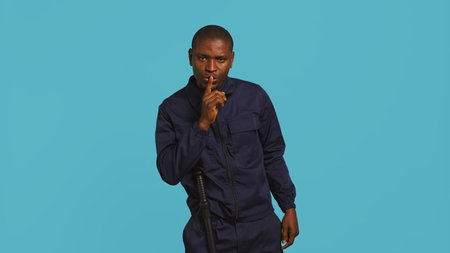 Portrait of security guard doing shush sign gesturing with finger to intruder while overseeing premises. Private law enforcement worker urging people to keep quiet, studio backdrop, camera Bの写真素材