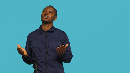 Portrait of security guard waiting for miracle, putting hands together while overseeing premises. Private law enforcement worker looking to sky, praying, studio backdrop, camera Aの写真素材