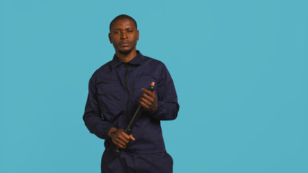 Portrait of security guard menacingly smacking hand with baton while overseeing premises. Private law enforcement worker cautioning trespassers with truncheon, studio backdrop, camera Bの写真素材