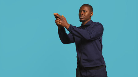 Portrait of security agent securing assigned post, pretending to shoot gun, studio background. African american guardian prepared to handle security breaches, doing pistol fingers gesturing, camera Bの写真素材