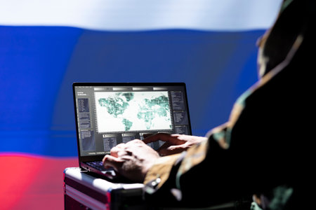 Russian military operative uses laptop to analyze surveillance data, standing isolated over Russia flag background. Kremlin regime agent engaged in geopolitical operation, protecting bordersの写真素材