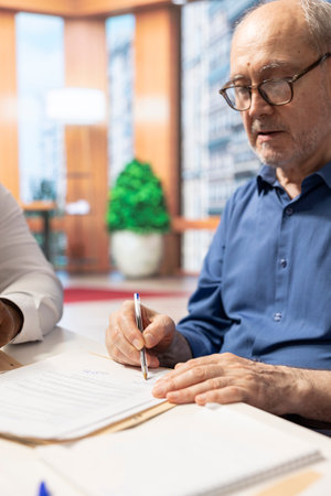 Elderly man gives his signature for the financial contract in modern office, signing a document to secure a retirement plan for his pension. Senior client receives counseling.の写真素材