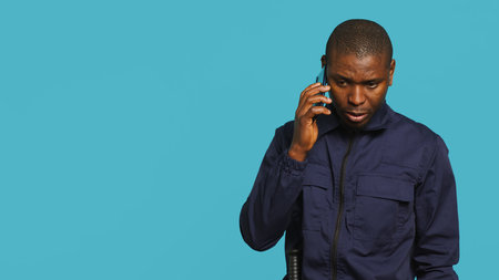 Security guard using smartphone, taking break during protection job shift. Portrait of bodyguard texting friends at work using mobile phone, isolated over studio background, camera Aの写真素材