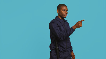 Portrait of security guard pointing finger at intruders while overseeing premises. Private law enforcement worker scolding unwanted trespassers, studio backdrop, camera Bの写真素材